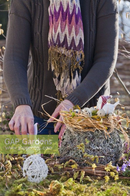 Femme créant un arrangement de Pâques en plein air avec un nid de paille et des œufs de caille.
