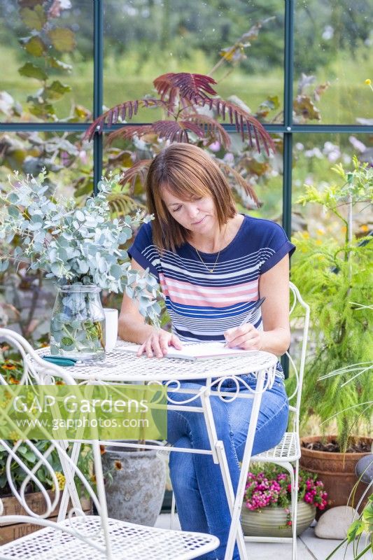 Femme assise à table écrit dans une serre remplie de plantes