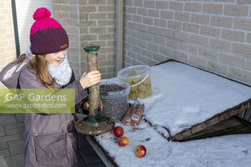 Fille tenant une mangeoire remplie de graines de tournesol le jour de la neige en hiver