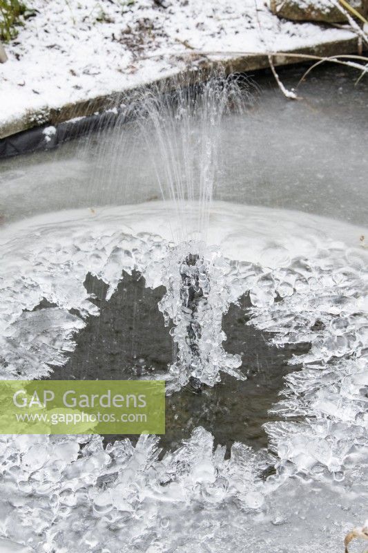 Fontaine à eau dans un bassin de jardin couvert de glace