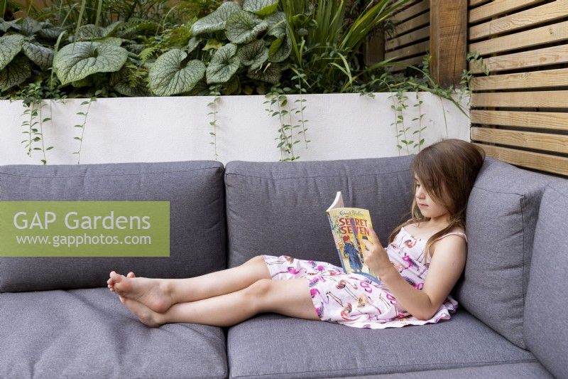 Jeune fille lisant un livre sur les sièges de jardin avec coussins.