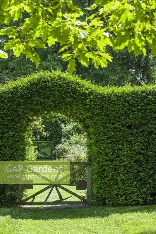 Portes en bois rustiques conçues par George Carter pour incorporer d'anciens outils de jardin et placées dans des ouvertures dans des haies d'ifs. Juin.