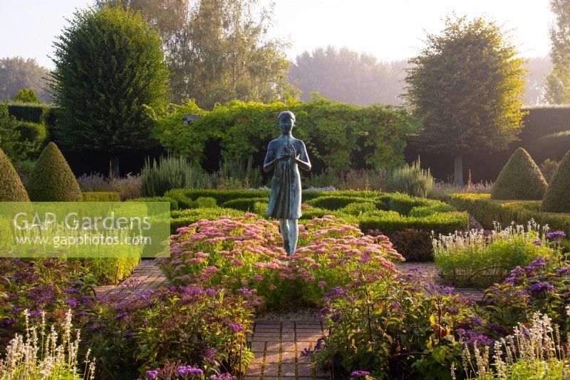 La statue de la Lampe de la Sagesse entourée de Sedum « Autumn Joy », d'Heliotropium arborscens et de topiaires Box and If dans le jardin à la française des Waterperry Gardens 
