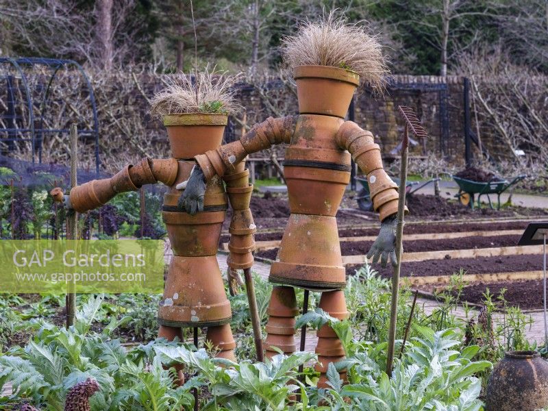 Une paire de jardiniers fabriqués à partir de pots en terre cuite se trouvent parmi des parterres de fleurs surélevés du RHS Rosemoor Garden en février. 