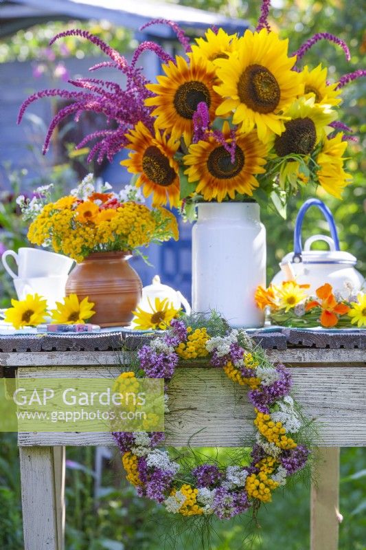 Couronne d'été et bouquets de tournesols, amarante, capucine, soucis en pot et tanaisie dans des vases sur la table. 