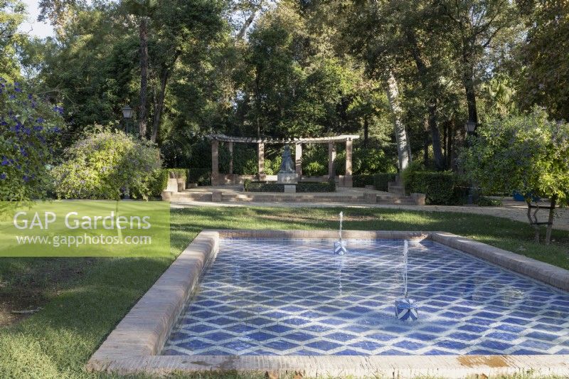 Une piscine carrelée bleu et blanc avec deux fontaines, une grande pergola incurvée est en arrière-plan. Parque de Maria Luisa, Séville, Espagne. Septembre 