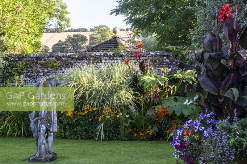 Les parterres de fleurs d'été et une statue dans le jardin de la piscine du Manoir, Little Compton. La plantation comprend le Miscanthus sinensis 'Variegatus', le Canna 'Roi Humbert' et le Tetrapanex 'Rex''. 