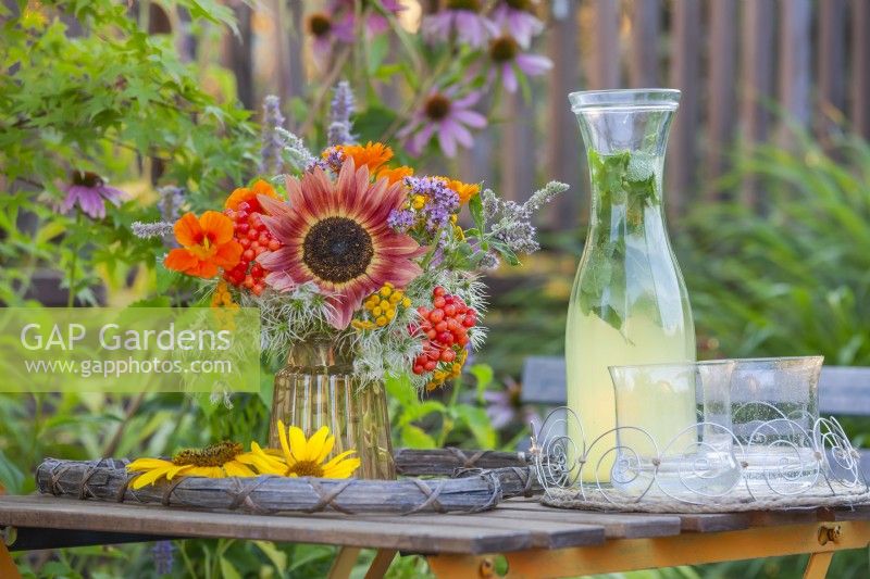 Boisson froide et bouquet d'été dans un vase en verre avec tournesols, têtes de graines de clématites, baies de rose de Guelder Tanacetum, Capucine et Mentha. 
