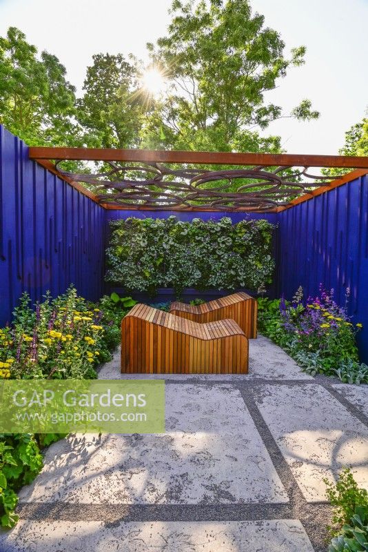 Relaxation area surrounded by a navy blue painted panels with decorative wooden deckchairs set against living green wall under with geometric design openwork of pergola roof. June
Bord Bia Bloom, Dublin
Designer: Jane McCorkell



