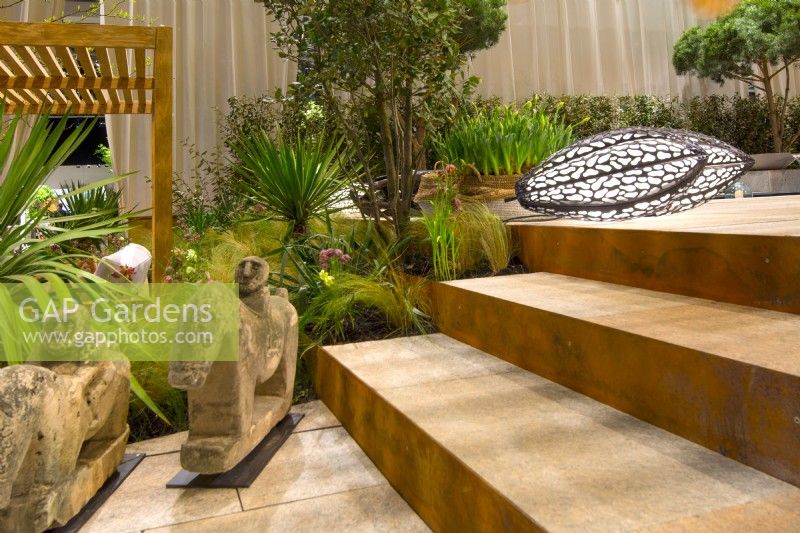  Steps made from natural stone near African sculpture and decorative floor lamp. Beyond a tropical-style border of Yuccas and Stipa tenusissima.
Designer: Vetschpartner, Berger Gartenbau and Livingdreams. Giardina-Zurich, Swiss. 

