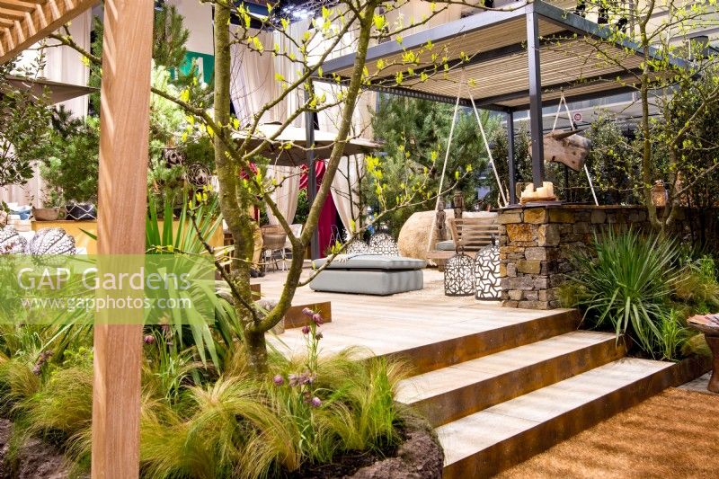 View of luxurious African seating area, a pergola with  swing surrounded by plants on raised beds: Stipa tenuissima, Fritillaria meleagris, Yucca gloriosa, Yucca filamentosa. 
Designer: Vetschpartner, Berger Gartenbau and Livingdreams. Giardina-Zurich, Swiss.





