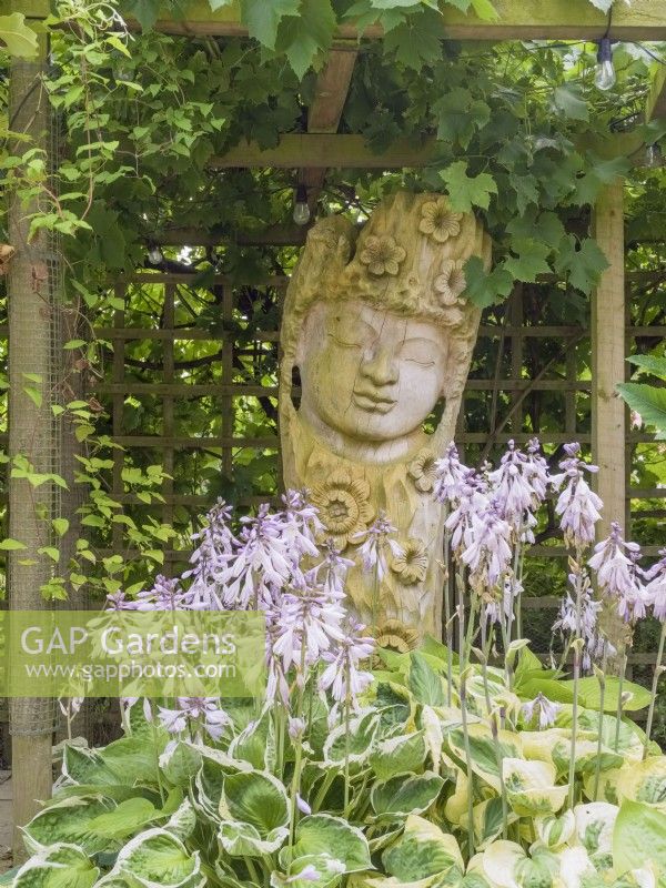 Hosta flowers and carved wooden Buddha head under pergola
