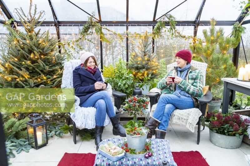 Women sitting in decorated greenhouse with hot drinks, talking