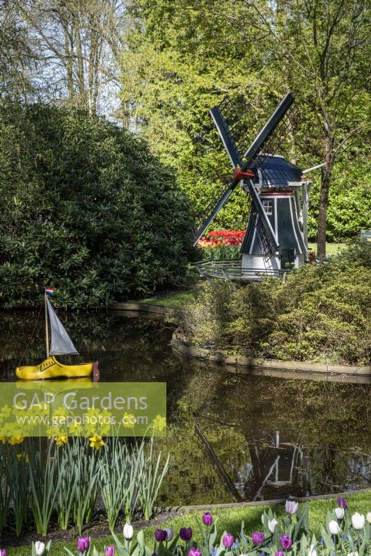 Vue sur l'eau des jardins de Keukenhof, aux Pays-Bas, au printemps. Un moulin à vent miniature derrière et un bateau « sabot » dans le jardin printanier 