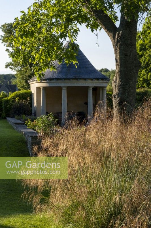 Maison d'été de style temple dans un jardin d'été avec Stipa gigantea, herbe d'avoine géante 