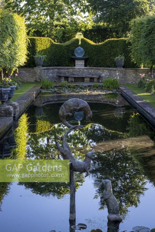 Des sculptures ornementales de loutres de Susie Wilson s'ébattent au-dessus d'un étang à la française qui reflète le jardin à la française environnant. 