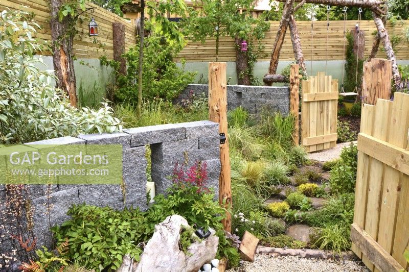 Opened wooden gates leading to grassy-gated dog area in the woodland inspired garden surrounded by a wooden planks fence with a decorative Connemara walling system. Planted with Astilbe, fungi, grasses. June
Designer: Mary Anne Farenden. Bord Bia Bloom, Super Garden, Dublin, Ireland.

