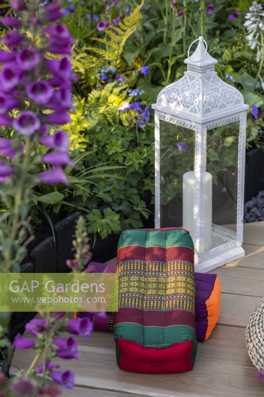 Tibetan meditation cushions and a metal lantern in a garden meditation corner surrounded by plants