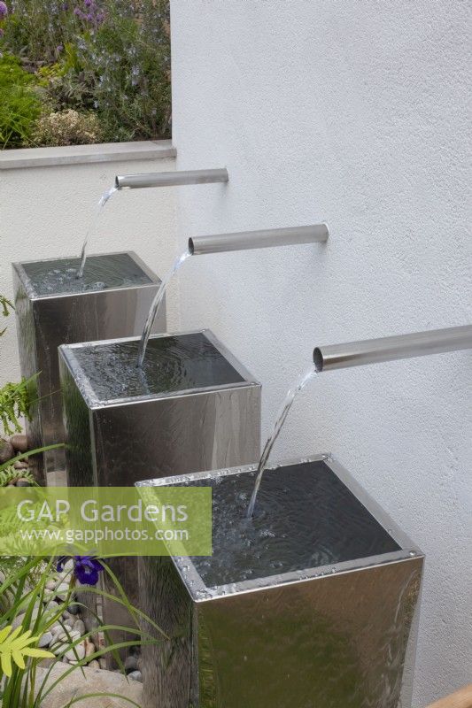 Three chrome water spouts cascading into metal containers in the 'Sociability' garden at BBC Gardener's World Live 2015, June