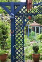 Vue d'ensemble du petit jardin de la cour densément planté regardant à travers le treillis bleu au pavillon d'été peint en vert.