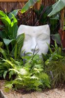 Sculpture de tête 'Bindi Dreamer' par Jilly Sutton, nichée parmi le feuillage vert de Cyperus papyrus et Dryopteris filix-mas - The Yoga Garden, médaillée de bronze au RHS Hampton Court Flower Show 2010