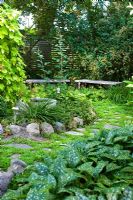 Jardin ombragé avec chemin pavé menant à travers Humulus lupulus - Golden Hop au centre, Leptinella squalida entre pavés, Pulmonaria, Hosta, Geranium, bancs et bain d'oiseaux