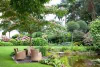 Coin salon sur terrasse en bois, la plantation comprend - Hydrangea macrophylla, Cedrus atlantica 'Pendula', Prunus fruticosa 'Globosa' et Albizia julibrissin - Tropical Touch