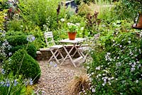Table et chaises peintes avec pot de géraniums blancs sur une petite terrasse en brique - Brook Hall Cottages, Essex NGS