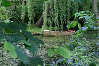 Vue depuis la promenade boisée d'un vieux bateau à rames en bois dans l'étang, à l'ombre d'un saule pleureur - Sallowfield Cottage B