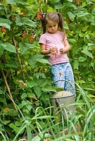 Jeune fille de cinq ans avec un arrosoir dans le jardin potager.
