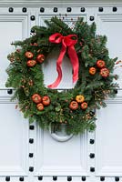 La belle vieille porte d'entrée est décorée d'une couronne de Noël traditionnelle et durable faite d'épicéa, avec des cynorrhodons rouges, des citrouilles séchées et du ruban.