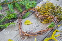 Un cœur de vigne sur une surface en bois, accompagné de feuillage d'if, de Prunus au lichen et de feuillage de conifère
