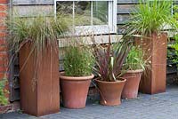Pots en terre cuite et en acier rouillé plantés de Phormium tenax, Deschampsia flexuosa et pennisetum graminées ornementales.