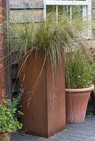 Un grand pot en acier rouillé déborde d'herbe ornementale Deschampsia flexuosa.