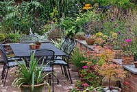 Un jardin de campagne sur deux niveaux avec un coin repas sur la terrasse, des parterres de fleurs surélevés avec des vivaces mixtes et des plantations en pot.