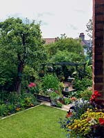 Une vue surélevée depuis la véranda, d'un petit jardin de ville en pente, conçu en diagonale pour 'tromper l'oeil' et maximiser la largeur. Cet effet est obtenu avec une pelouse décalée, un étang et une terrasse en bois.