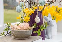 Affichage floral contenant des œufs décoratifs, des jonquilles, un feuillage printanier en fleurs et un lapin, en vue du jardin