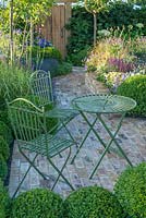 Table et chaises en fer forgé sur dallage en briques entourées de balles topiaires - Squire's Garden Centres Urban Oasis - RHS Hampton Court Flower Show 2015