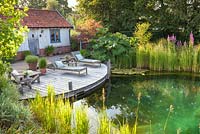 Scène d'été tranquille avec étang de baignade, fauteuils inclinables et terrasse en bois.