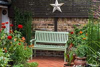 Un banc en bois peint entouré de pots plantés de zinnia, tithonia et gaillardia aux couleurs chaudes.