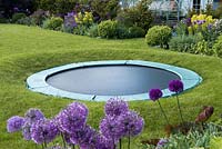 Un trampoline installé dans un cercle de pelouse surélevé de façon à ce qu'il soit largement caché à distance.