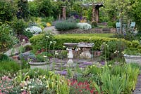 Un jardin à 4 niveaux en terrasses dont un jardin d'herbes aromatiques avec thym intercalé avec dallage, haie de buis, pelouse, coin salon et parterres de fleurs mixtes colorés.