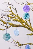 Décorations en argile peinte avec des empreintes de feuillage de pin, suspendues à une branche recouverte de lichen