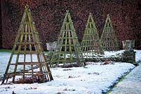 Parterres herbeux recouverts de neige avec des obélisques pyramides en bois à Levens Hall and Garden, Cumbria, Royaume-Uni.