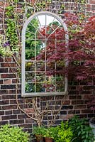 Un miroir en forme de fenêtre réfléchissant la lumière dans une cour.