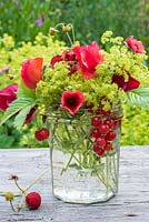 Arrangement floral d'été dans un bocal en verre avec pois de senteur rouges, Potentialla, Fragaria Vesca, groseilles rouges et alchemilla mollis