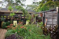 Plan large d'un parterre de jardin d'un chalet qui regarde en arrière vers la maison entourée d'un mur de bois autoportant recyclé, avec des pots montés sur les murs plantés de plantes succulentes.