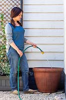 Femme utilisant un tuyau pour remplir un grand pot pour créer un étang.