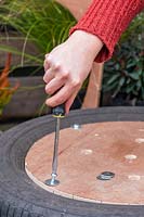Femme utilisant des rondelles et des boulons pour fixer la base en bois sur le semoir à pneus.