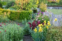 Voir le long du parterre de fleurs, avec Paeonia - pivoine, Iris barbata - iris barbu et Taxus - if - soutenu par une clôture en châtaignier.